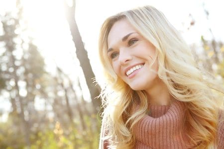 A woman smiling while outside among the trees.